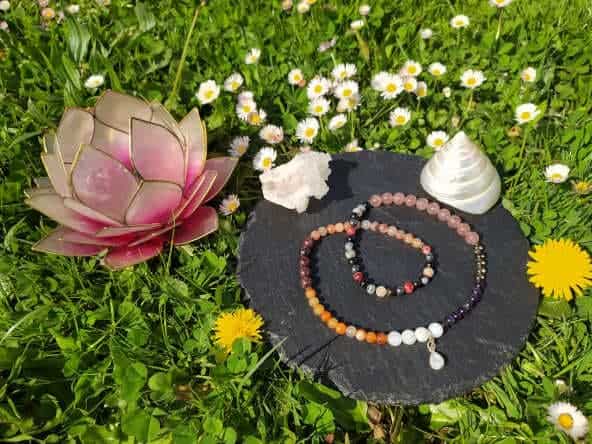 Mala lunaire personnalisé en présentation sur une plaque d'ardoise, avec un coquillage nacré et un bougeoir fleur en nacre, dans les fleurs au soleil